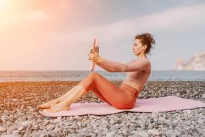 mujer mar pilates deportivo contento medio Envejecido mujer practicando aptitud en playa cerca mar, sonriente activo hembra formación con anillo en yoga estera afuera, disfrutando sano estilo de vida, armonía y meditación foto