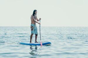 Man Sup Sea. Strong athletic man learns to paddle sup standing on board in open sea ocean on sunny day. Summer holiday vacation and travel concept. Aerial view. Slow motion photo