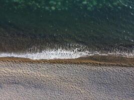 Aerial view from above on azure sea and pebbles beach. Small waves on cristal clear water surface in motion blur. Nature summer ocean sea beach background. Nobody. Holiday, vacation and travel concept photo