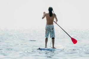 Man Sup Sea. Strong athletic man learns to paddle sup standing on board in open sea ocean on sunny day. Summer holiday vacation and travel concept. Aerial view. Slow motion photo