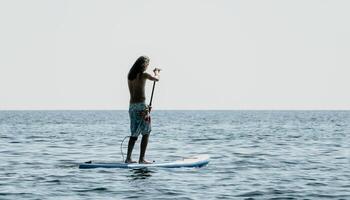 Man Sup Sea. Strong athletic man learns to paddle sup standing on board in open sea ocean on sunny day. Summer holiday vacation and travel concept. Aerial view. Slow motion photo