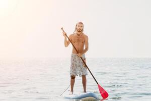 Man Sup Sea. Strong athletic man learns to paddle sup standing on board in open sea ocean on sunny day. Summer holiday vacation and travel concept. Aerial view. Slow motion photo