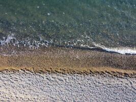 Aerial view from above on azure sea and pebbles beach. Small waves on cristal clear water surface in motion blur. Nature summer ocean sea beach background. Nobody. Holiday, vacation and travel concept photo