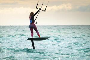 Young Caucasian woman athlete ride on a hydrofoil board with a kite in the open ocean. Hydrofoil is a new direction in kitesurfing photo
