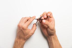 Man's hands doing a manicure. Scissors cutting fingernails on a hand on a white background photo