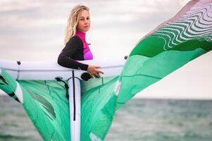 Portrait of a young female kitesurfer in a wetsuit holding her kite and looking at the camera against the background of the sea and sky photo