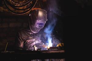 man in a welding mask welds a pipe in a dark workshop. welding smoke in the face, close-up photo