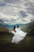 A newlywed couple, a man and a woman, are on a wedding walk in the mountains against the backdrop of rocky mountain peaks and a mountain lake. A man carries his wife in his arms photo