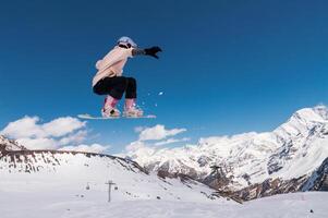 young woman snowboarder jumping from a springboard in the snowy mountains photo