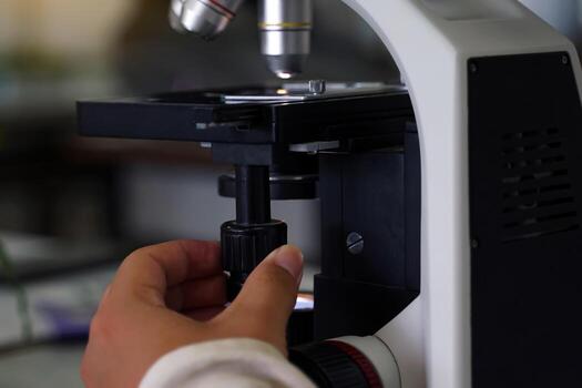 Hand turns the microscope's fine focus adjustment knob to increase the sharpness of the image. microscope is a piece of equipment in a science laboratory used to enlarge small images. photo