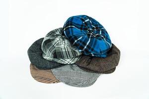 Stack of classic wool newsboy caps in different colors and patterns on a white background. Classic hats that were popular in the 50s are stacked for photos in the catalogue