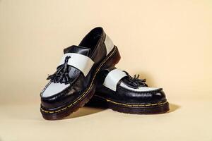 Isolated photo of an elegant and shiny two-tone vintage shoe product on a beige background. Close up of black and white tassel shoes with rubber outsole made from genuine cowhide.