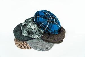 Stack of classic wool newsboy caps in different colors and patterns on a white background. Classic hats that were popular in the 50s are stacked for photos in the catalogue