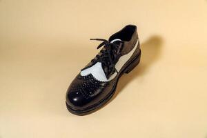 Close up of black and white brogue wingtip shoes with rubber outsole made of genuine cowhide. Studio shot of an elegant and shiny vintage two tone shoe product on a beige background photo