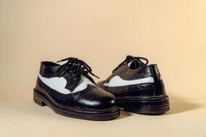 Close up of black and white brogue wingtip shoes with rubber outsole made of genuine cowhide. Studio shot of an elegant and shiny vintage two tone shoe product on a beige background photo