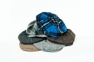 Stack of classic wool newsboy caps in different colors and patterns on a white background. Classic hats that were popular in the 50s are stacked for photos in the catalogue