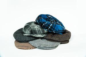 Stack of classic wool newsboy caps in different colors and patterns on a white background. Classic hats that were popular in the 50s are stacked for photos in the catalogue