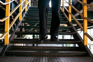 Close-up view of full black wingtip brogue shoes made of genuine leather worn by a male model in a deserted warehouse. Concept photo of classic wingtip brogue shoes in an old building made of iron