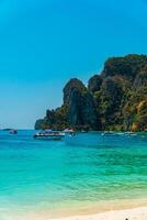 Large rock cliff covered in green trees with the sea in front of it on a sunny day. The view of large rock cliffs and vast ocean is a tourist icon for tropical islands in Krabi, Thailand photo