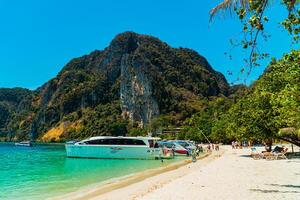 Large rock cliff covered in green trees with the sea in front of it on a sunny day. The view of large rock cliffs and vast ocean is a tourist icon for tropical islands in Krabi, Thailand photo