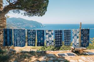 Beautifully patterned blue fabrics hanging on a clothesline under a tree, set against a peaceful mountain backdrop near the sea. photo