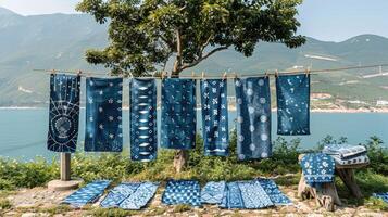 Beautifully patterned blue fabrics hanging on a clothesline under a tree, set against a peaceful mountain backdrop near the sea. photo