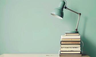Stack of books on a beige table with a pastel sage green background with a desk lamp photo
