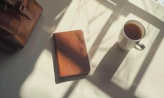Closed notebook on a white table with a cup of coffee and a handbag photo