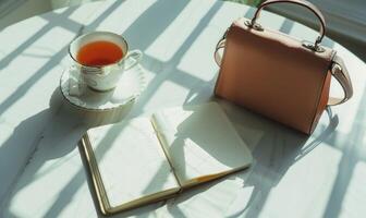 Closed notebook on a white table with a cup of coffee and a handbag photo
