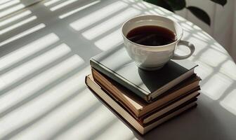 Stack of books on a light gray table with a cup of tea next to it photo