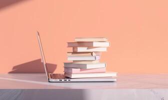 Stack of books on a light gray table with a pastel peach background, with a laptop beside photo