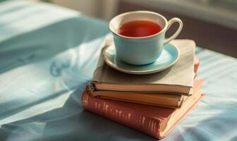 Stack of books on a light gray table with a cup of tea next to it photo