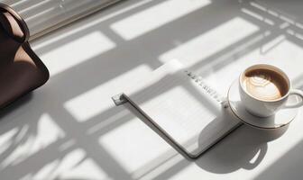 Closed notebook on a white table with a cup of coffee and a handbag photo