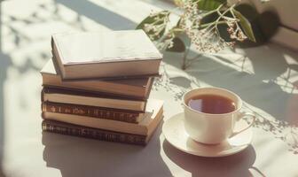 Stack of books on a light gray table with a cup of tea next to it photo