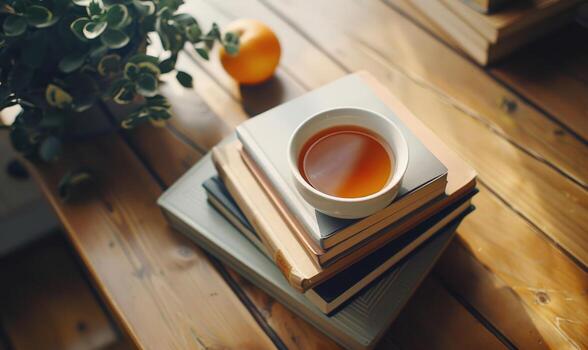 Stack of books on a wooden table with a cup of tea next to it, shadow from window, top view photo