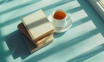 Stack of books on a light blue table with a cup of tea next to it, shadow from window, top view photo