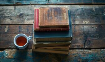 Stack of books on a wooden table with a cup of tea next to it, shadow from window, top view photo
