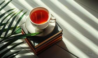 Stack of books with a cup of tea on a light gray table, soft shadows from window photo