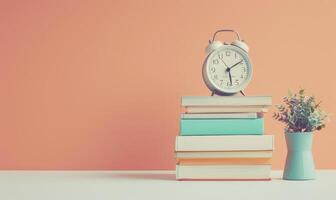 Stack of books on a white table with a pastel peach background, with a clock photo