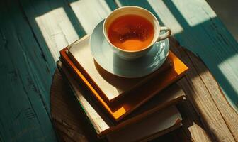 Stack of books with a cup of tea on a white table, window casting shadows photo