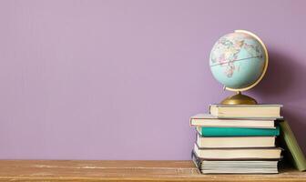 Stack of books on a wooden table with a pastel lilac background, with a small globe photo