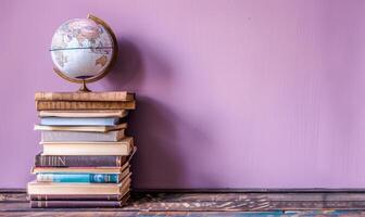 Stack of books on a wooden table with a pastel lilac background, with a small globe photo