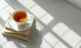 Stack of books with a cup of tea on a light gray table, soft shadows from window photo