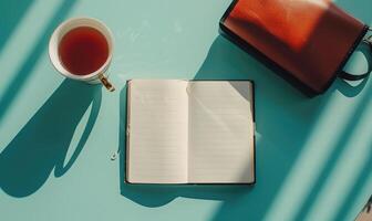 Notebook on a light blue table with a cup of tea, shadow from window photo