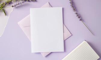 White blank card in a purple frame on a pastel periwinkle table, with a sprig of lavender and a small notebook photo