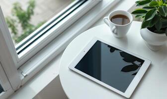 Tablet on a light gray table with a cup of tea on the left, sunlight from window photo