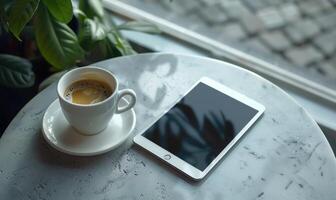Tablet on a light blue table with a cup of tea on the right, shadow from window, top view photo