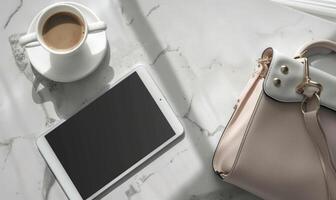 Tablet on a light blue table with a cup of tea on the right, shadow from window, top view photo