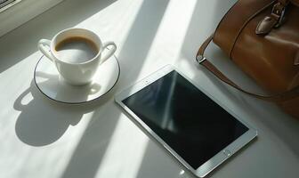 Tablet on a light gray table with a cup of tea on the left, sunlight from window photo