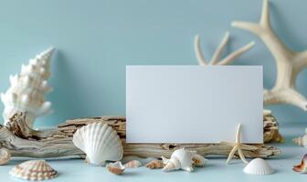 White blank card on a pastel sky blue background, with a small collection of seashells and a piece of driftwood photo